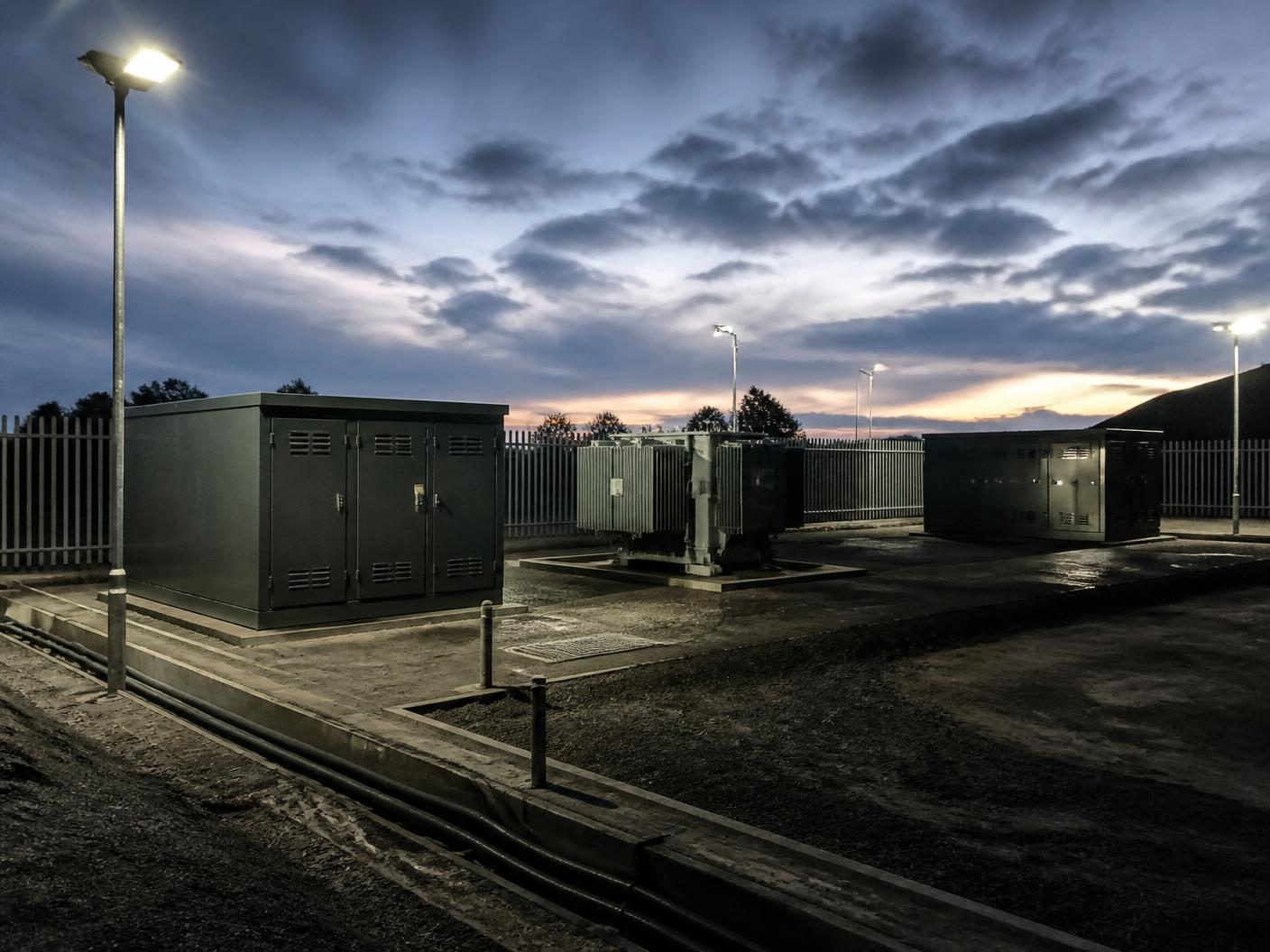 Floodlit outdoor substation compound with switchgear kiosks and a transformer